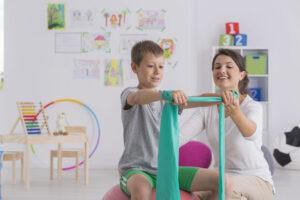 Physiotherapist,And,Boy,Sitting,On,A,Gym,Ball,Exercising,With 3